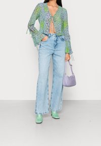 Translucent green and purple patterned top with tie front; light blue high-waisted flared jeans; mint green heels; small lavender bag.