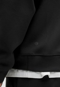 Felpa nera realizzata in tessuto morbido, con una vestibilità comoda e un logo discreto nella parte bassa della schiena. Stratificata con un dettaglio di indumento bianco all'orlo.