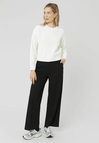 Pull en tricot côtelé blanc à col rond associé à un pantalon large noir et des baskets de sport argentées. Design simple et épuré.