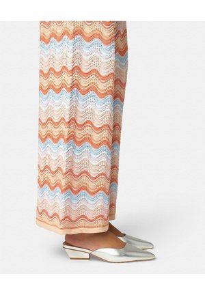 Falda hasta la pierna con patrón ondulado multicolor, llevada con zapatos mule plateados de tacón bajo y punta puntiaguda sobre un fondo claro.