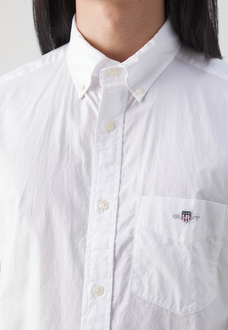 Chemise blanche à col pointu, dotée d'une poche poitrine avec un logo brodé. Fabriquée en tissu légèrement texturé.
