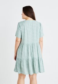 Light green dress with short sleeves, featuring a tiered skirt and white leaf patterns, made of a soft, textured fabric.