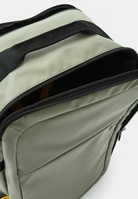 Zaino in tessuto grigio con accenti neri, dotato di apertura con zip, struttura imbottita e spazio interno visibile. Superficie testurizzata.