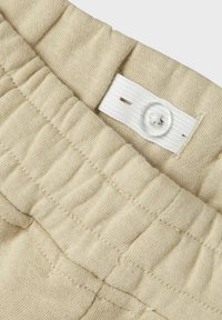 Beiga shorts med texturerat tyg, elastisk midja och vit knappstängning med en sydd etikett. Passar för avslappnad klädsel.