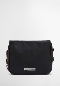 Mala mensageiro preta com um detalhe em pele castanha, apresentando um fecho de aba e uma etiqueta com o logótipo. Feita de material durável com uma textura suave.