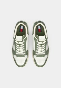 Baskets de sport vertes et blanches avec un embout perforé, un laçage symétrique, une semelle en caoutchouc et une doublure intérieure de marque avec des accents rouges et bleus.