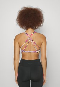 Urheiluliivit, joissa on monivärinen kukkakuosi ja ristikkäinen takanauha. Yhdistetty korkeavyötäröisten mustien legginsien kanssa.