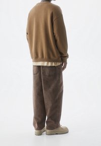 Brun sweatshirt med avslappnad passform, lager-på-lager över en ljus t-shirt. Matchas med lösa bruna byxor och beiga skor. Slät textur.