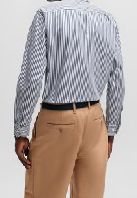 Randig långärmad skjorta i marinblått och vitt, kombinerad med ljusbruna byxor med sidofickor och knäppning på baksidan.