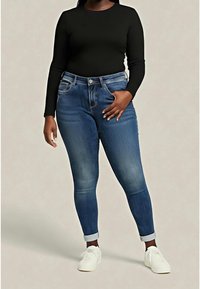 Top de manga larga oscuro, vaqueros azules de cintura alta con un ligero desgaste, ajuste ceñido y puños doblados, combinados con zapatillas blancas.