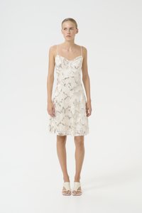 Kreemikas kleit, millel on vormiv kehaosa ja laienev seelik, mis on kaunistatud läikiva maod meenutava mustriga, õhukeste rihmadega ja üle põlve pikkusega.