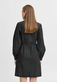 Robe en denim noir avec des manches bouffantes, un corsage ajusté et une jupe évasée, présentant des coutures détaillées et une texture lisse.