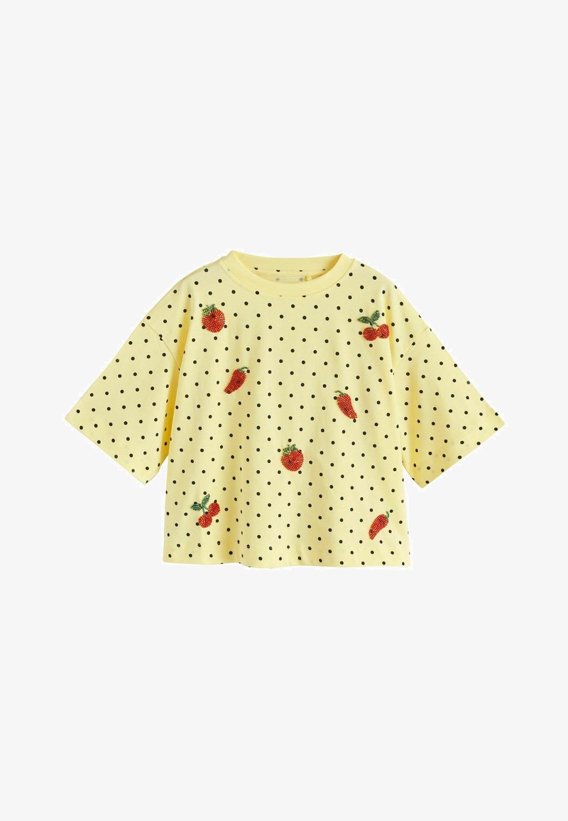 Chemise jaune à manches courtes avec des pois noirs et des motifs brodés de fruits et légumes rouges dispersés sur le devant.