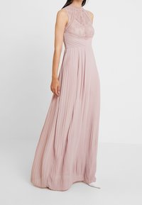 Blush roze maxi-jurk met een geplooide rok, kant bodice en hoge hals. Heeft een aansluitende taille en een mouwloze ontwerp. Gladde textuur.
