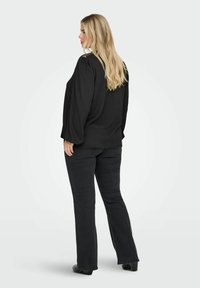 Czarna, oversize'owa bluzka z bufkami, zestawiona z ciemnymi dzwonami. Materiał wydaje się być textured; wygląd jest casualowy i wygodny.