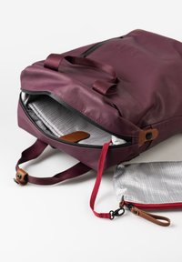 Zaino di un intenso bordeaux con un'esterno liscio, maniglie superiori e chiusura con zip. L'interno presenta una fodera a quadretti grigia e una piccola tasca.