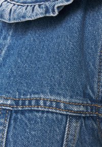 Denim fabric close-up featuring a frilled collar, blue color, textured weave, visible stitching in orange, and subtle fading at seams.
