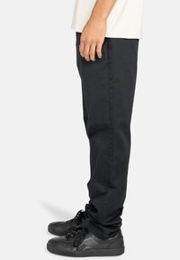 Sorte bomuldsbukser med lige pasform, har sidelommer og bæres med sorte sneakers, vist fra en sidevinkel.