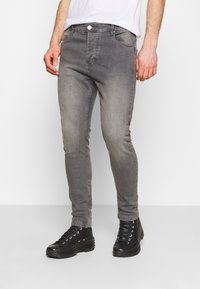 Gray denim jeans with a slim fit, featuring a faded finish, five pockets, and a button fly, paired with black lace-up boots.