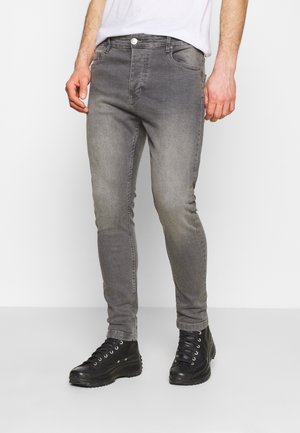 Jeans de mezclilla gris con un corte ajustado, que presentan un acabado desgastado, cinco bolsillos y un cierre de botones, combinados con botas negras de cordones.