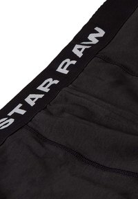 Črne boksarice z mehkimi vlakni, ki imajo širok elastičen pas z napisom "STARRAW" v belih črkah.