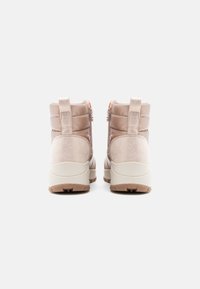 Botas aislantes beige con un acabado de ante texturizado y sintético liso, punta redonda y suela de goma baja. Incluyen una cremallera y una pestaña de tirón.