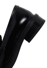 Zapato de charol negro con punta redondeada y un tacón bajo y grueso. Presenta costuras visibles y una superficie suave y brillante.