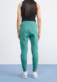 Pantaloni felpa verdi realizzati in tessuto morbido, con un design a gamba affusolata e una vita elasticizzata, abbinati a scarpe da ginnastica bianche.