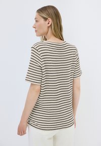 Kurzärmliges, gestreiftes Oberteil in Creme und Schwarz mit gerippter Textur und Rundhalsausschnitt, in lockerer Passform und standard Länge.