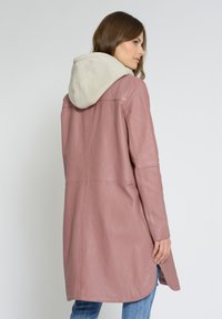 Vaaleanpunainen nahkatakki, jossa on ristikkäinen beige huppu, hieman A-linjainen leikkaus, sivuaukot ja sileä pinta.