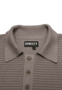 Vaaleanruskea neulottu poolopaita, jossa on tekstuuri, kolme nappia ja käännettävä kaulus. Etiketissä lukee "HONESTY RULES," koko L.