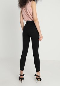 Jeans negros de tiro alto con un diseño ajustado, combinados con un top sin mangas rosa. La modelo lleva tacones negros con acentos de lazo.