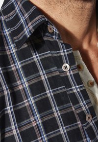 Kariertes Hemd mit einem dunkelblauen Grundton und weißen, roten und gelben Linien. Button-Down-Kragen mit runden Knöpfen und weicher Textur.