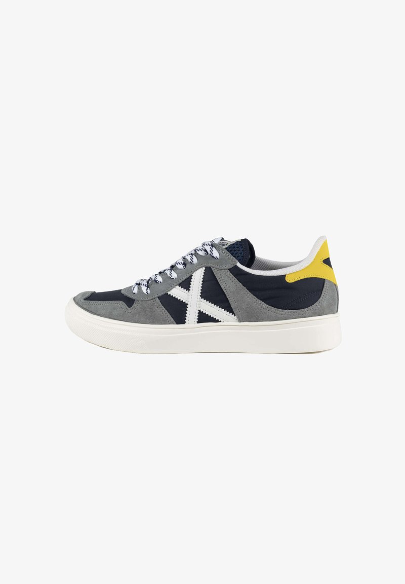 Grey and navy leather sneaker with white laces, textured suede, rubber sole, and yellow heel accent. Features a white star design on the side.