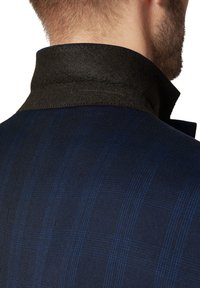 Marynarska granatowa kurtka w kratę z kołnierzem wykończonym ciemnobrązowym filcem. Tkanina ma subtelną teksturę i linie w wzór siatki.