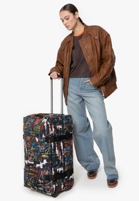 Rullväska med ett färgglatt graffiti-mönster på svart bakgrund, med justerbara remmar och ett utfällbart handtag.