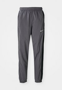Nike track pants, made of lightweight fabric, in dark gray with black side panels. Features an elastic waistband and reflective logo.