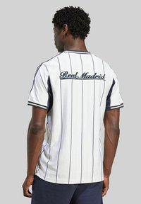 Jersey de rayas blancas con "Real Madrid" bordado en la parte posterior. Con detalles en azul marino en las mangas y el escote, fabricado con una tela suave y ligera.