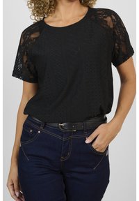 Svart t-shirt med spetsdetaljer i överkant och korta ärmar, parat med mörkblå denimjeans och ett svart bälte.