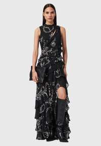 Czarna sukienka bez rękawów z białym kwiatowym wzorem, warstwowe falbany, wysoki rozcięcie, w połączeniu z czarną kopertówką i czarnymi połyskującymi kozakami za kolano.