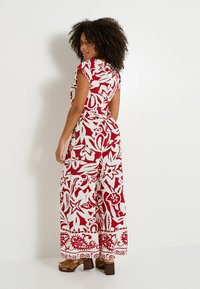 Mono floral rojo y blanco con mangas cortas y cinturón en la cintura, con piernas anchas y un dobladillo estampado, combinado con tacones gruesos marrones.