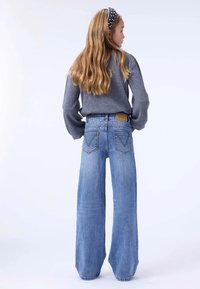 Jean large bleu clair à taille haute, avec un patch de marque et des poches arrière ornées de coutures décoratives. Pull gris inclus.