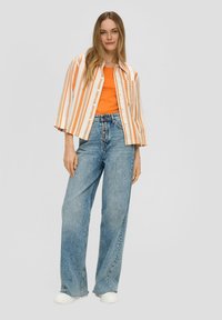 Oranje gestreepte korte mouwen blouse over een oranje tanktop, gecombineerd met lichtblauwe hoge taille wijde jeans en witte sneakers.