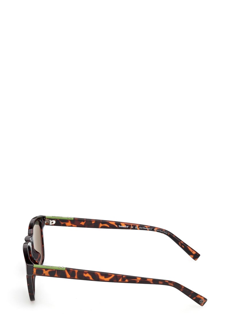 Lunettes de soleil écaille de tortue avec des montures rectangulaires et épaisses. Accent vert sur les branches intérieures et verres sombres. Fini de surface texturé.