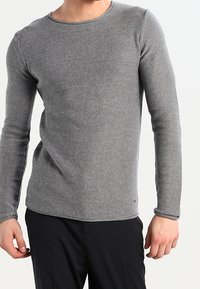 T-shirt à manches longues en maille côtelée de couleur gris moyen. Doté d'un col rond et d'une coupe ajustée. La texture du tissu est douce et légèrement extensible.