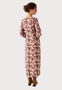 Vestido largo rosa con estampados florales blancos, mangas largas y silueta recta. Combinado con botines de ante marrón.