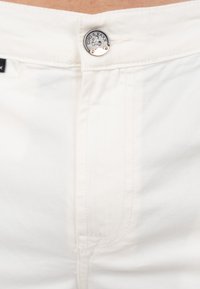 Witte katoenen denim met een knoopsluiting in de taille. Kenmerkt zich door eenvoudige stiksels en een aansluitend ontwerp, close-up van het bovenste gedeelte.