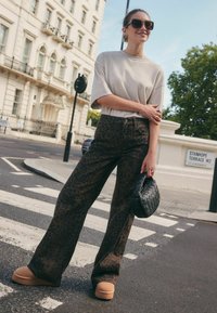 Bruine panterprint brede pijpenbroek, losse beige top met korte mouwen, zwarte geweven handtas en stevige tan platform schoenen. Stedelijke straatsetting.