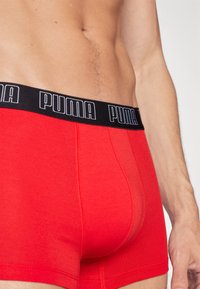 Boxers rouges en tissu doux avec une ceinture noire portant le logo "PUMA" en blanc. Le design comprend un avant sans couture.