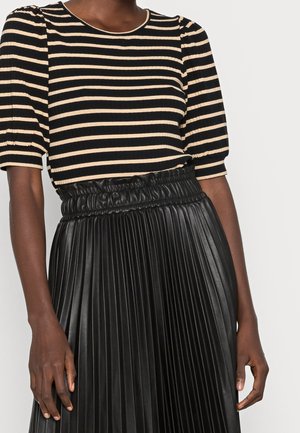 Femme portant un haut à manches courtes rayé horizontal noir et beige, rentré dans une jupe plissée noire taille haute avec une ceinture froncée.